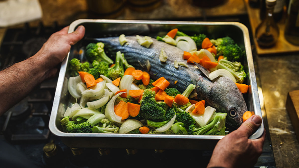 Mãos a segurar travessa de forno com peixe e legumes